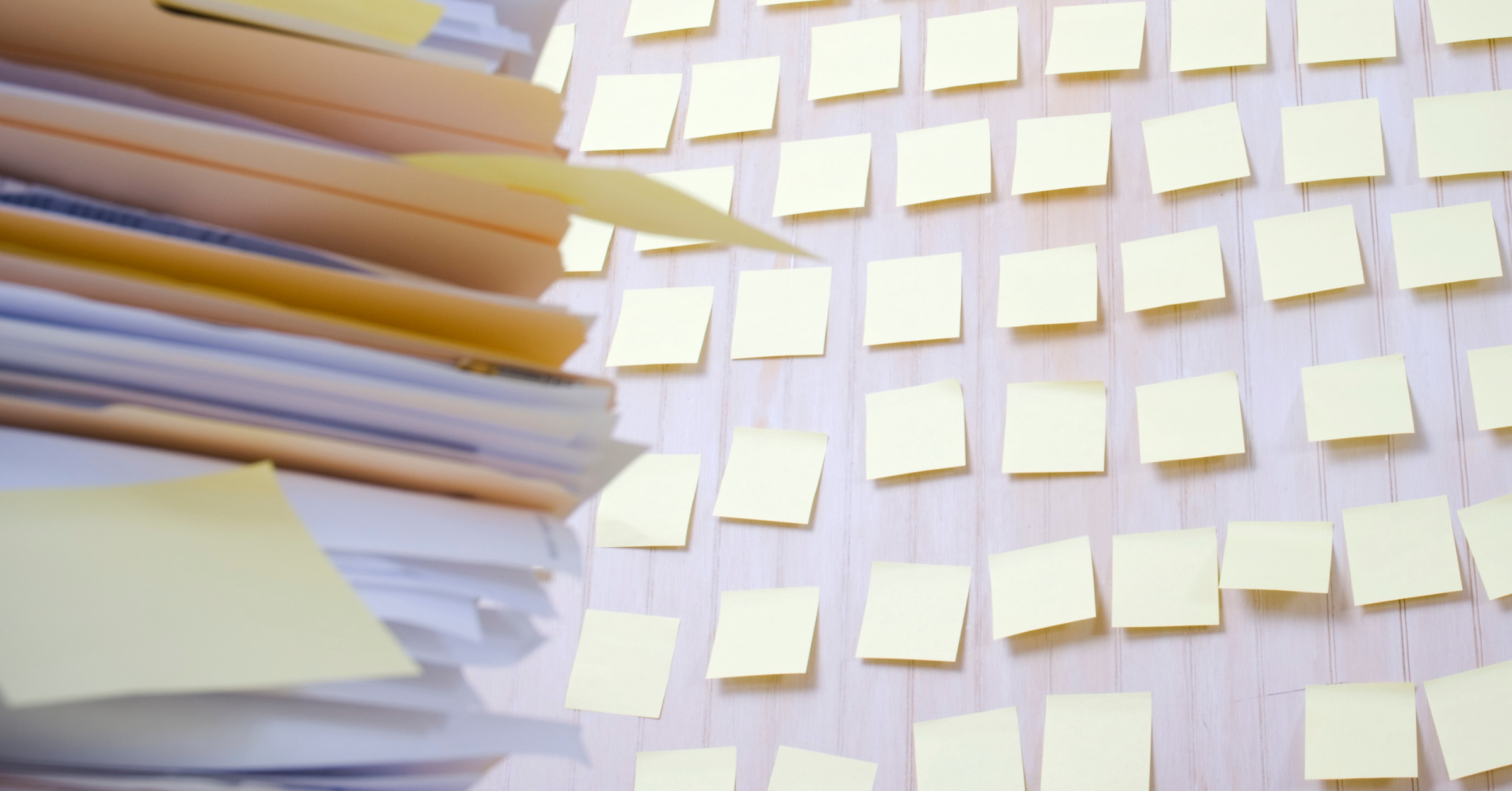 Tall stack of documents and file folders next to dozens of sticky notes on a wall, representing invoice review workflows, administrative workloads, compliance tracking, and document management challenges.